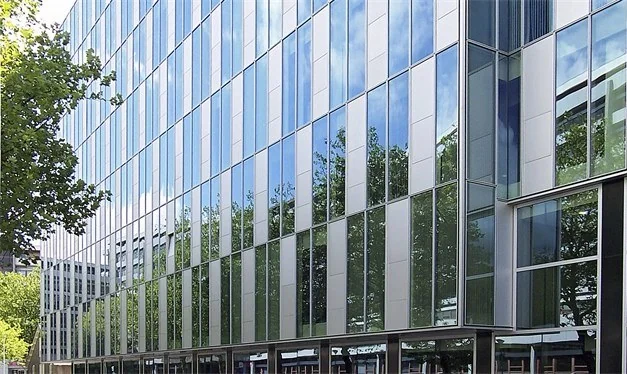 Moderne glazen gevel van een kantoorgebouw aan de Benthemstraat met reflectie van bomen en lucht.