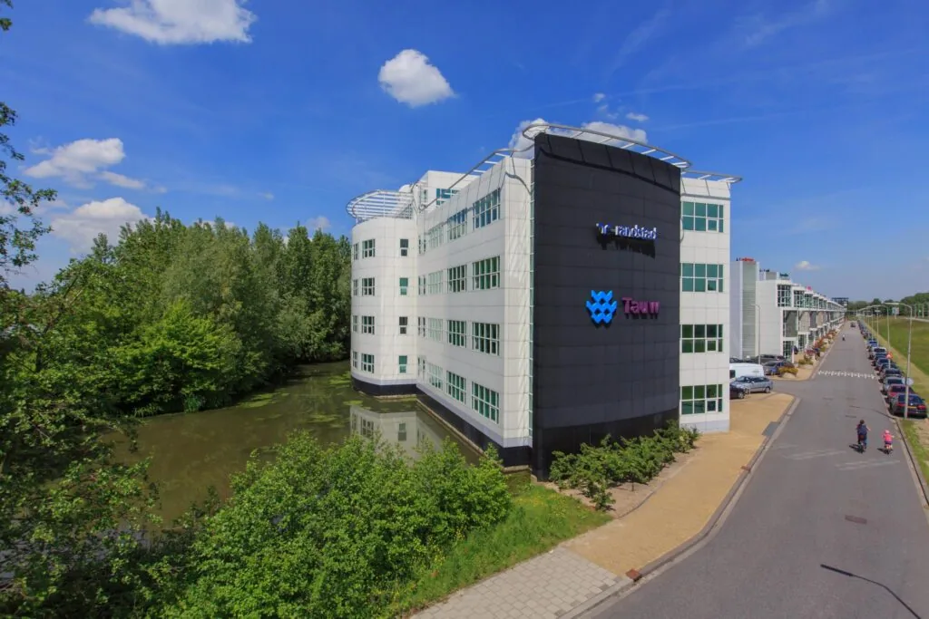 Modern kantoorgebouw van Tauw aan het Rhijnspoor, gelegen naast water en een groenstrook.