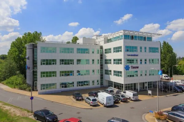 Wit kantoorgebouw aan de Rhijnspoor met de logo’s van Tauw en Randstad op de gevel en een parkeerplaats op de voorgrond.