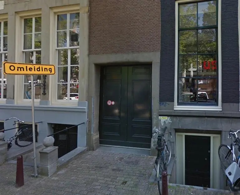 Geel omleidingsbord bij een pand aan de Keizersgracht met fietsen en grote groene deuren.