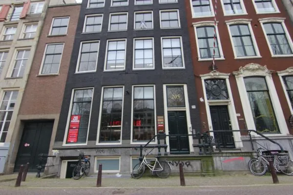 Voorgevel van een zwart grachtenpand aan de Keizersgracht 205 in Amsterdam, met fietsen voor de deur en een "We are hiring"-poster in het raam.