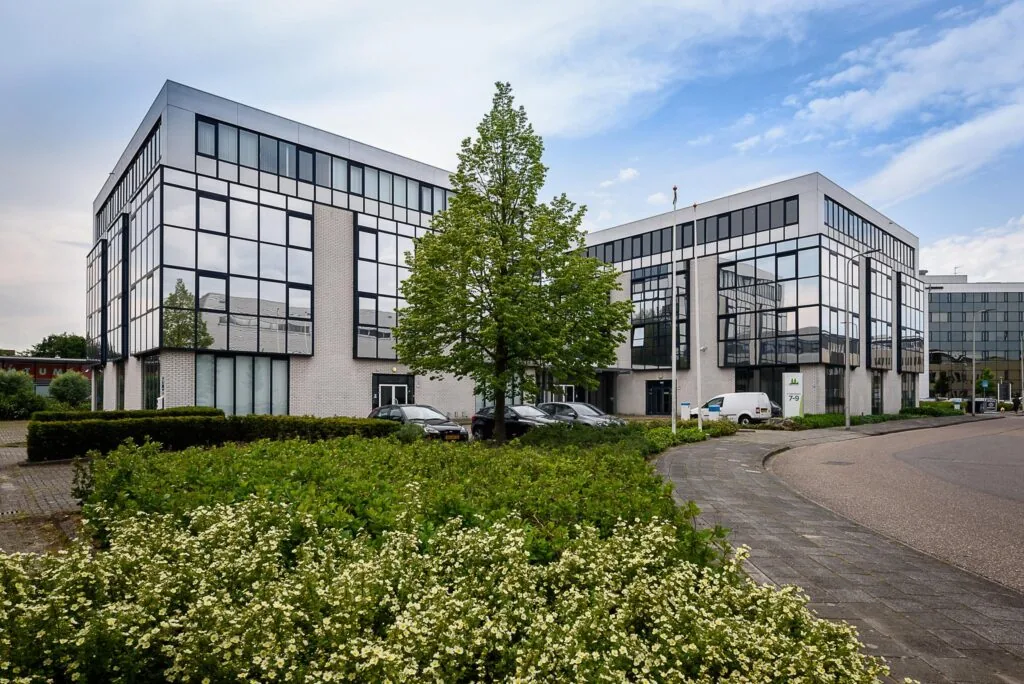 Modern kantoorgebouw aan de Cypresbaan met spiegelende ramen, parkeervakken en omliggend groen.