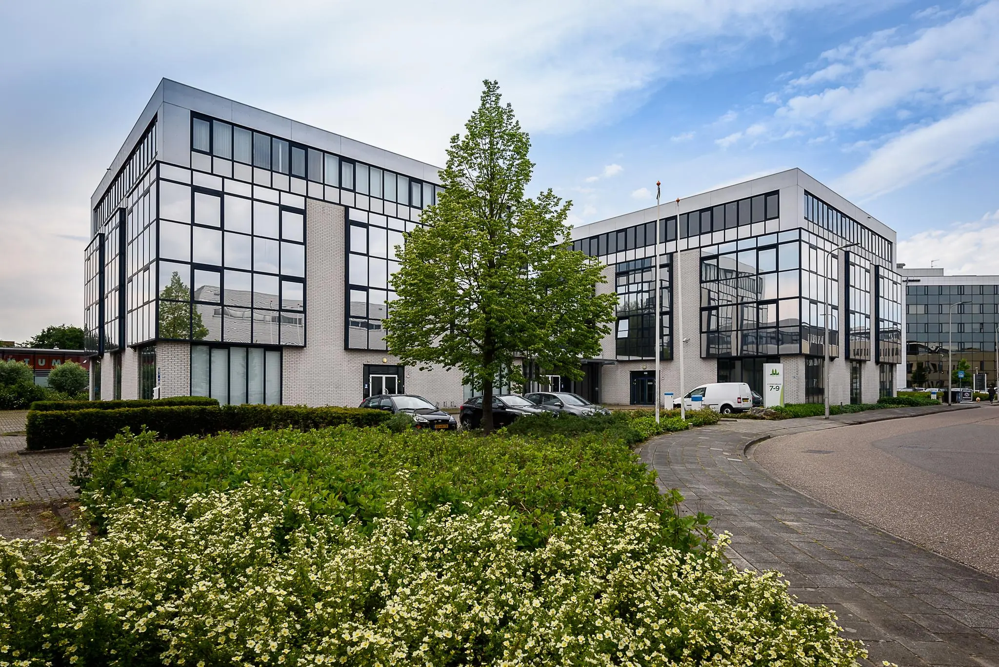 Modern kantoorgebouw aan de Cypresbaan met spiegelende ramen, parkeervakken en omliggend groen.