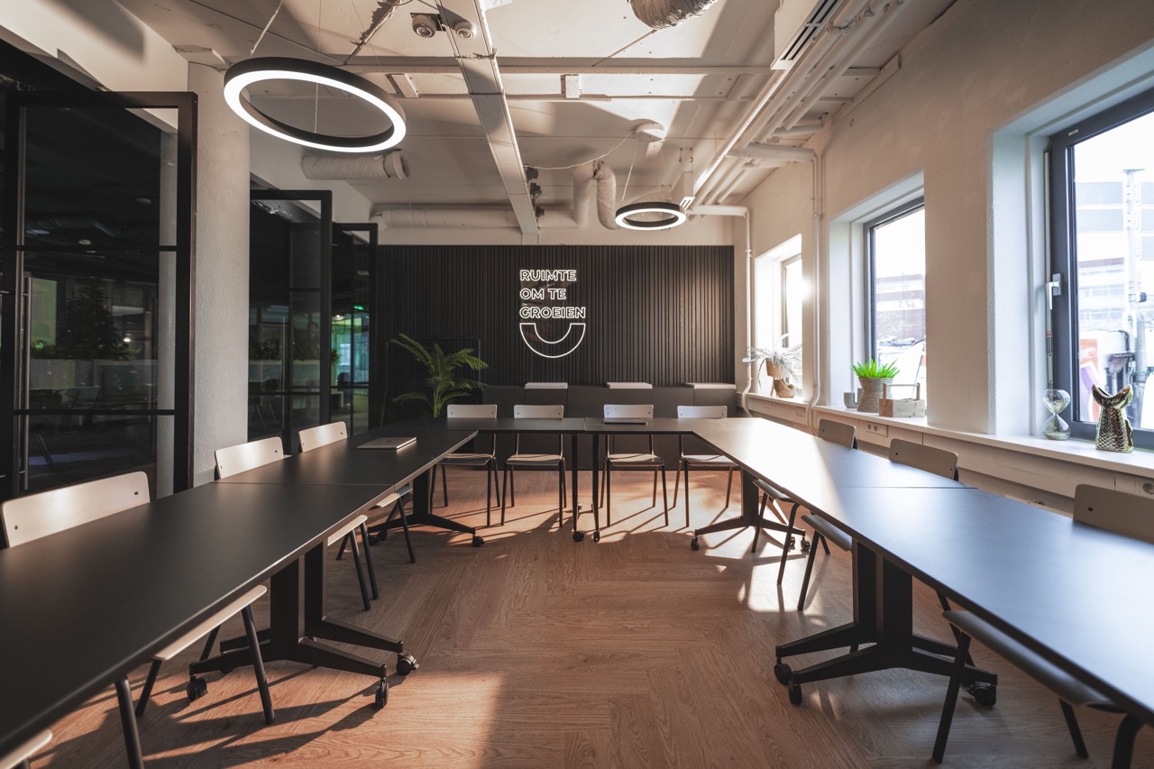 Moderne vergaderruimte met U-vormige opstelling, houten vloer en de tekst "Ruimte om te groeien" op de achterwand.
