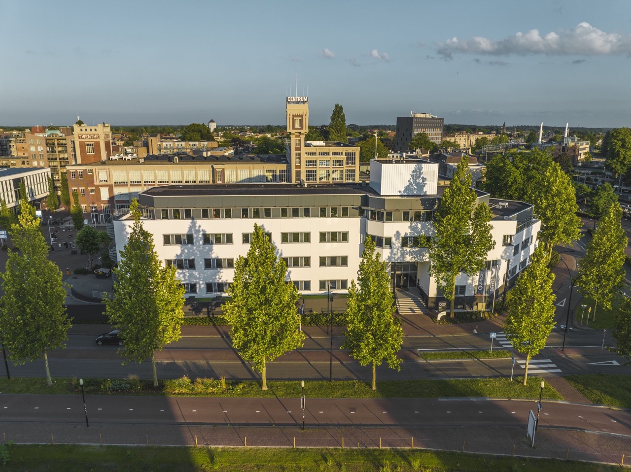 Luchtfoto van een modern wit kantoorgebouw aan een met bomen omzoomde straat in het centrum van een stad.