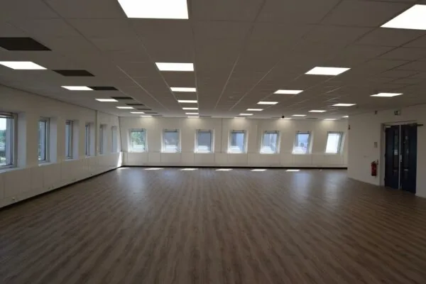 Lichte, lege ruimte met houten vloer, systeemplafond en meerdere ramen in een gebouw aan de Twentestraat.