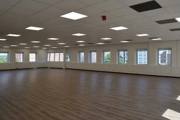 Ruime, leegstaande kantoorruimte aan de Twentestraat met houten vloer, systeemplafond en grote ramen die uitzicht bieden op omliggende gebouwen.