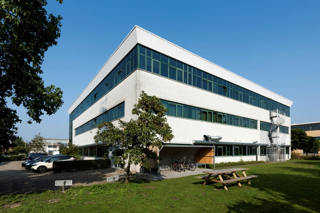 Modern kantoorgebouw aan de Zekeringstraat met parkeerplaatsen, fietsenstalling en picknickbank op een grasveld.