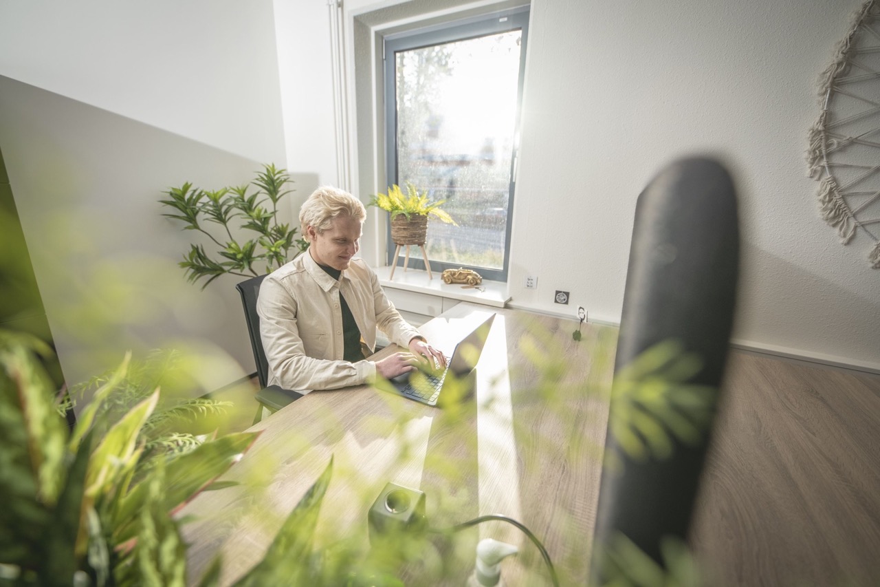 Man werkt op een laptop in een modern, licht kantoor met veel planten.