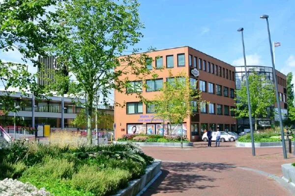 Modern kantoorgebouw aan het Stationsplein, omringd door groen en bestrate wandelpaden.