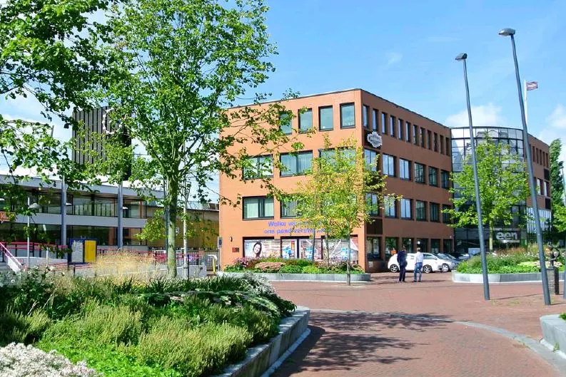 Modern kantoorgebouw aan het Stationsplein, omringd door groen en bestrate wandelpaden.