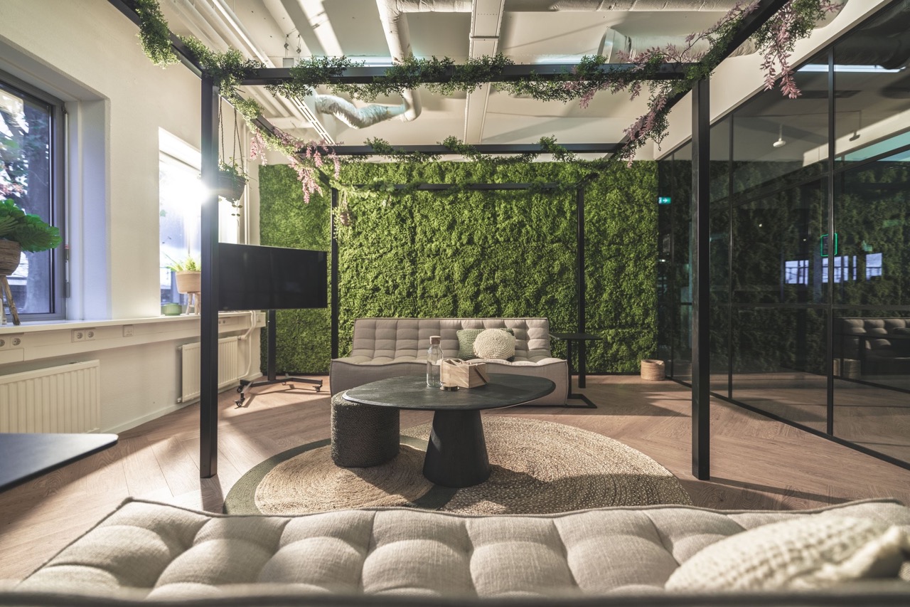 Modern ingerichte loungeruimte met groene moswand, comfortabele zitbanken en een ronde salontafel.