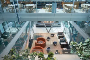 Moderne, open kantoorlobby aan de Amstelveenseweg met zithoeken, tafels en glazen wanden op meerdere verdiepingen.