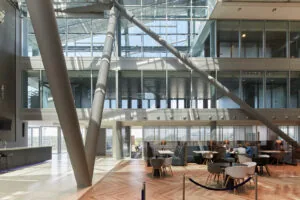 Moderne kantoorlobby aan de Amstelveenseweg met hoge glazen gevels, zitgedeeltes en opvallende stalen steunpilaren.