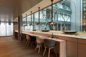 Moderne werkruimte met hoge stoelen aan een lange houten tafel, uitkijkend op een glazen binnenhof aan de Amstelveenseweg.