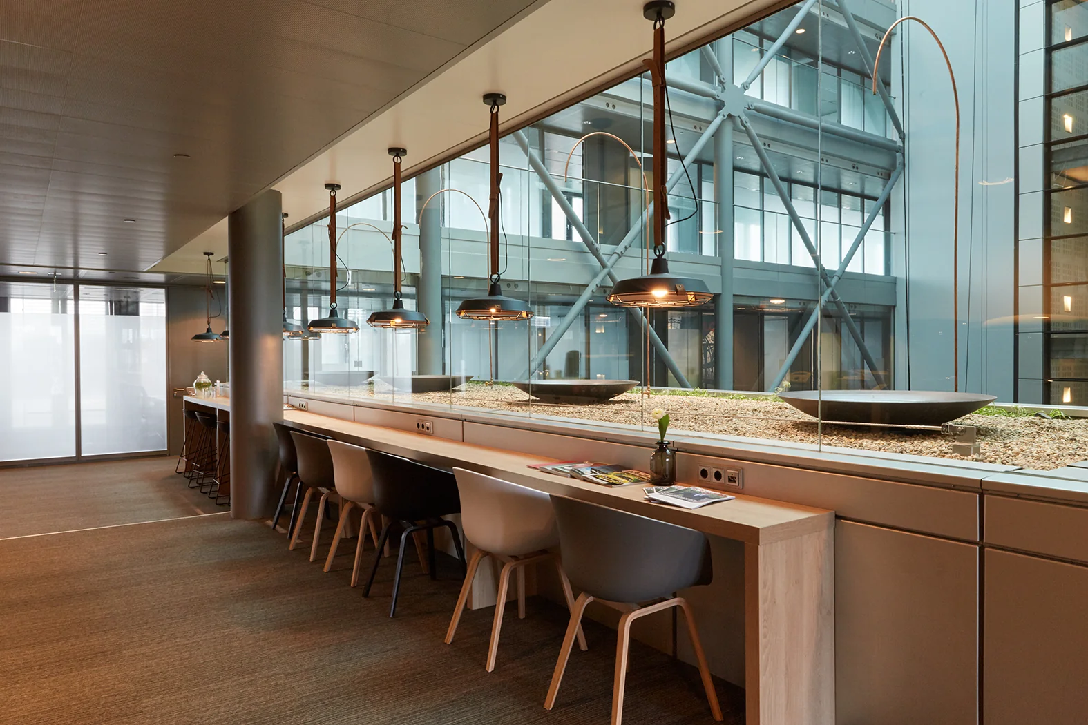 Moderne werkruimte met hoge stoelen aan een lange houten tafel, uitkijkend op een glazen binnenhof aan de Amstelveenseweg.
