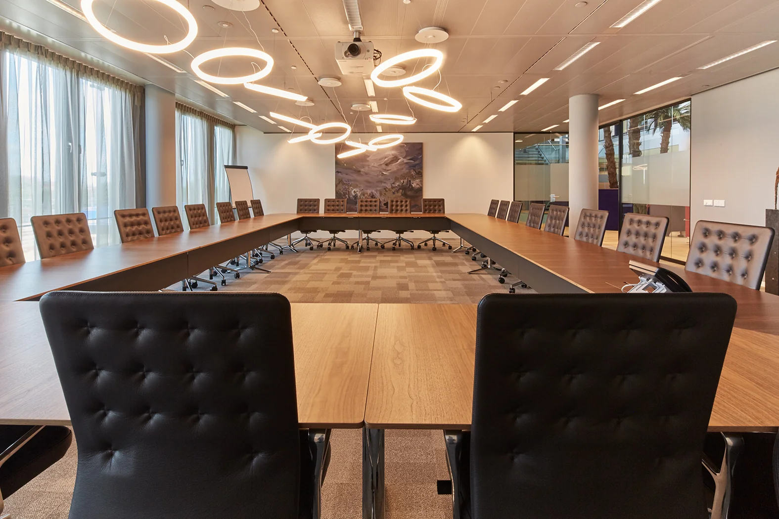 Moderne vergaderruimte aan de Amstelveenseweg met een U-vormige tafelopstelling, luxe stoelen en opvallende ringvormige plafondverlichting.