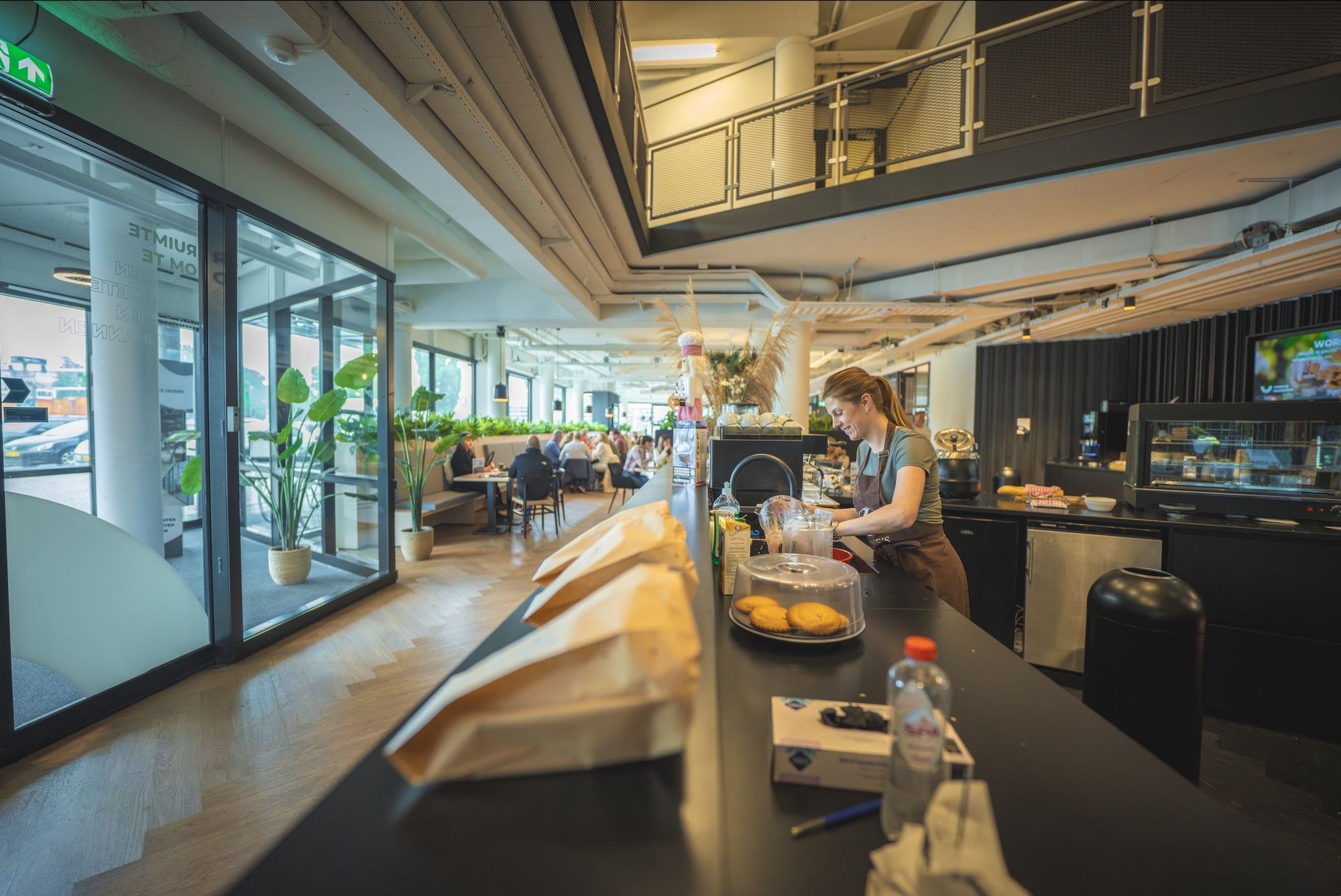 Barista bereidt drankjes in een modern en levendig café met zitplaatsen en planten.