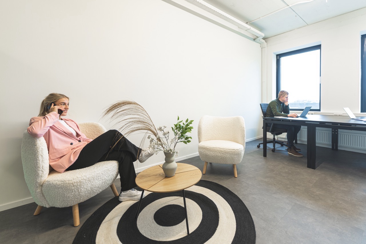 Twee mensen werken in een modern kantoor van Dreesz, één aan een bureau met laptop en de ander zittend in een stoel terwijl ze telefoneert.