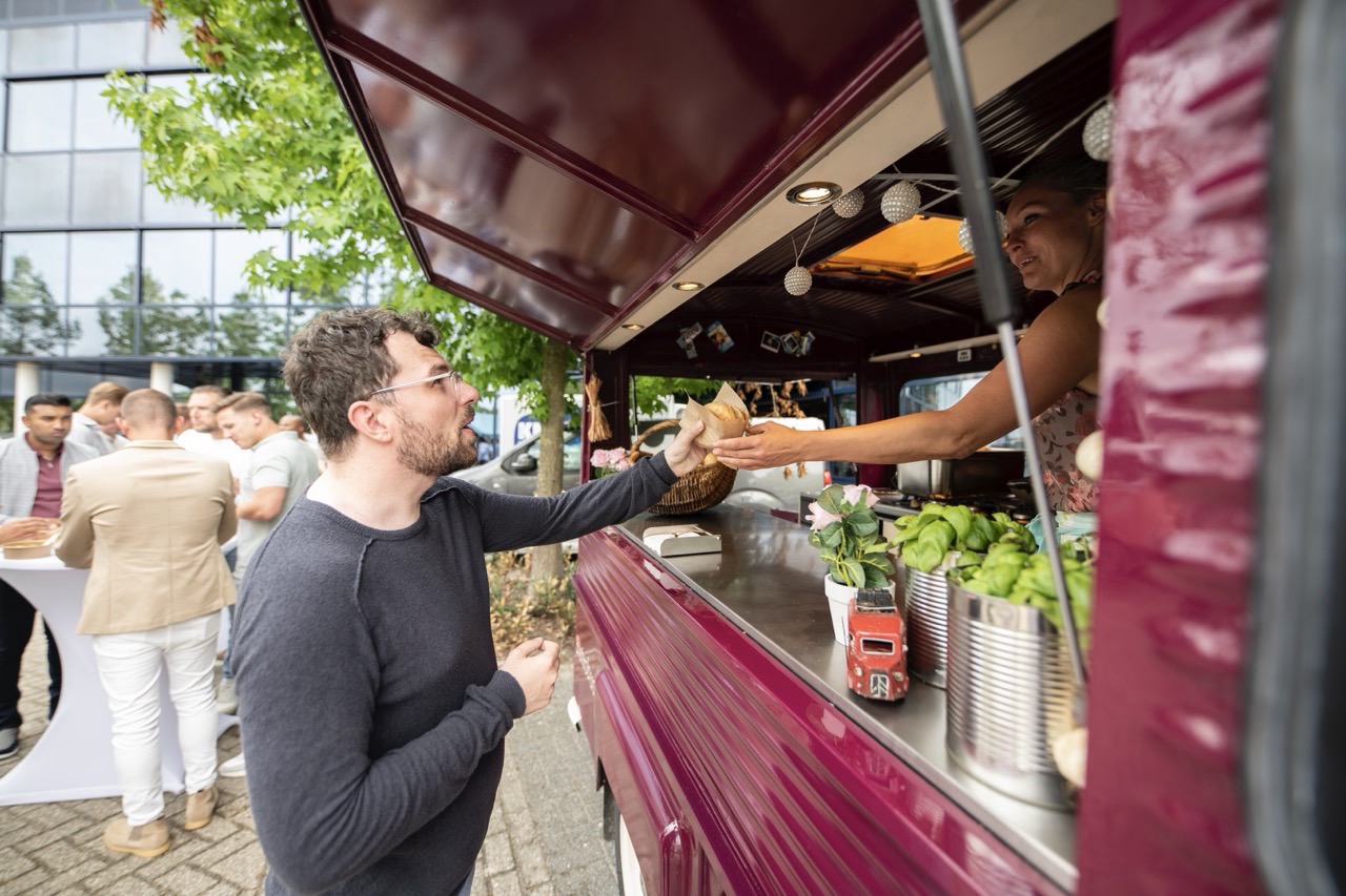 Man ontvangt een gerecht bij een paarse foodtruck tijdens het evenement Workspace Rally 2023.