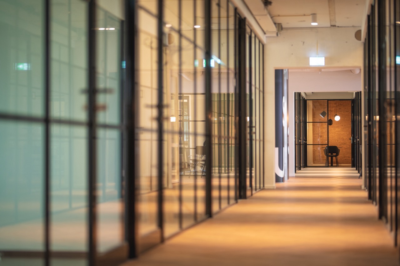 Lange, moderne gang met glazen kantoordeuren en een eenzame stoel aan het einde.