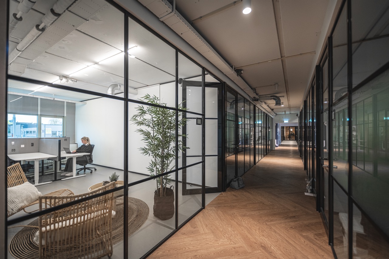 Flexplek in Delta 2 met glazen wanden, houten vloer en een vrouw werkend aan een bureau.