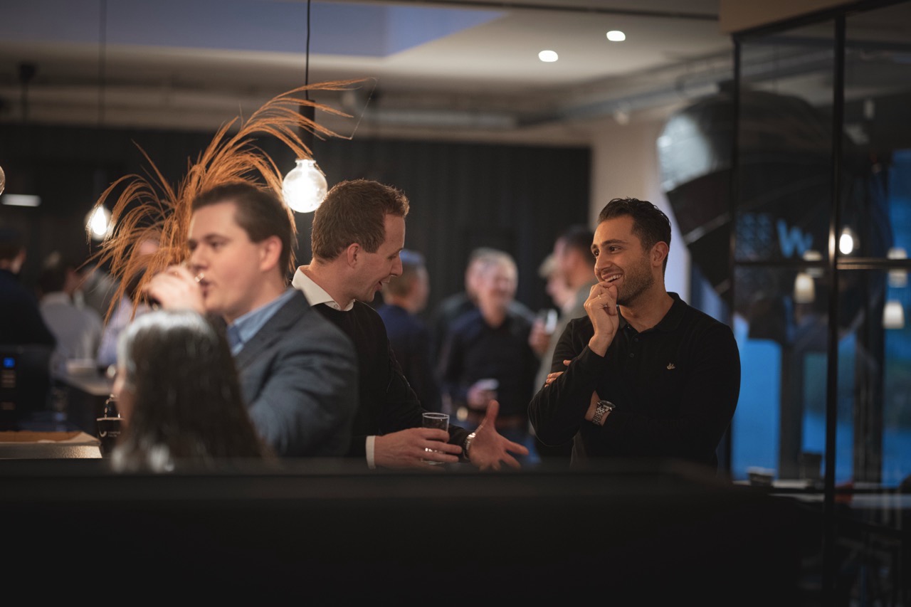 Mensen in gesprek en genietend van drankjes tijdens een netwerkevenement in een sfeervol verlichte ruimte.