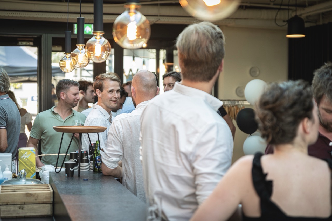 Groep mensen praat en drinkt samen tijdens de Workspace Rally 2022 in een gezellige, modern verlichte ruimte.