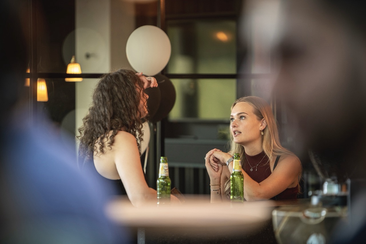 Twee vrouwen zitten aan een tafel met bierflesjes en praten tijdens het evenement Workspace Rally 2022.