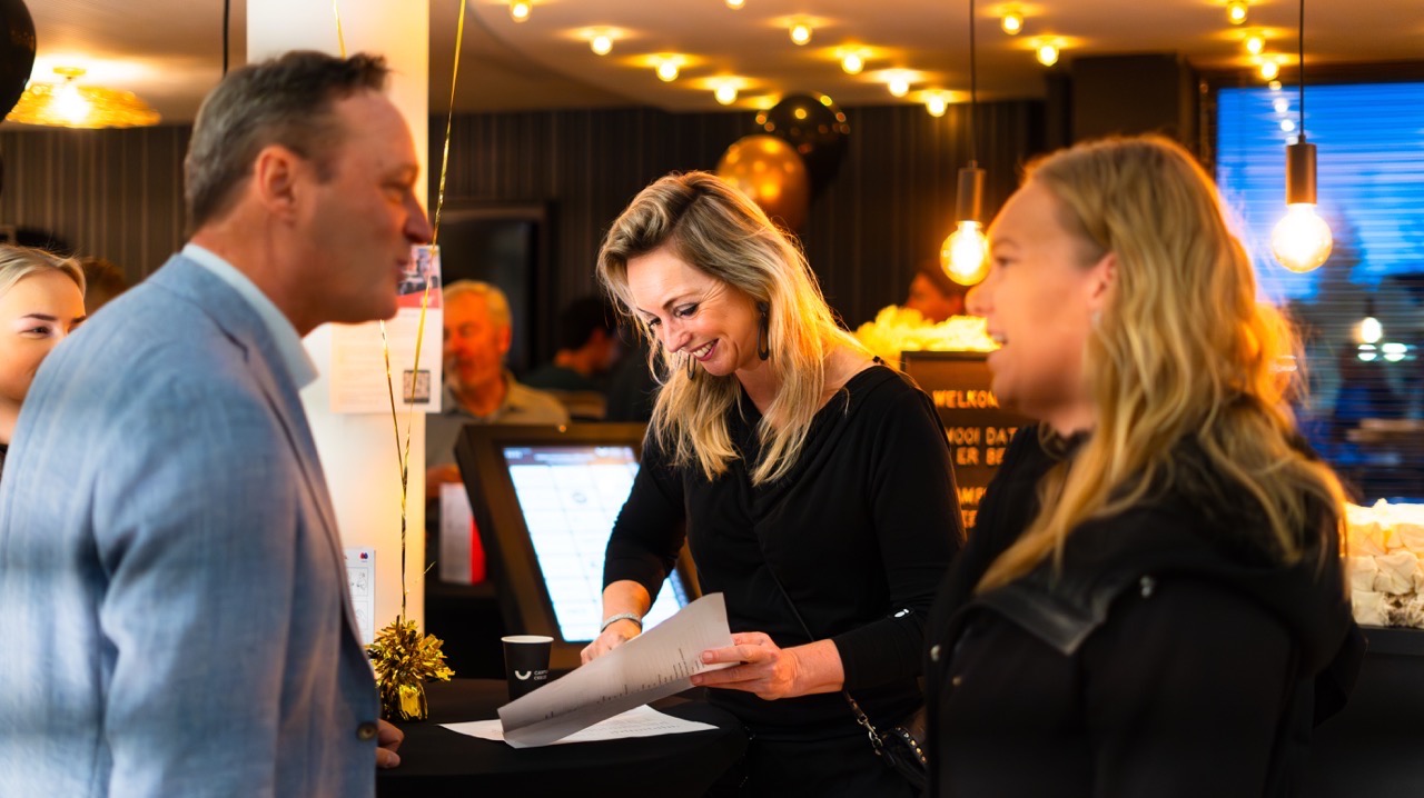 Vrolijke mensen in gesprek bij een ontvangstbalie tijdens een feestelijke gelegenheid met warme verlichting.