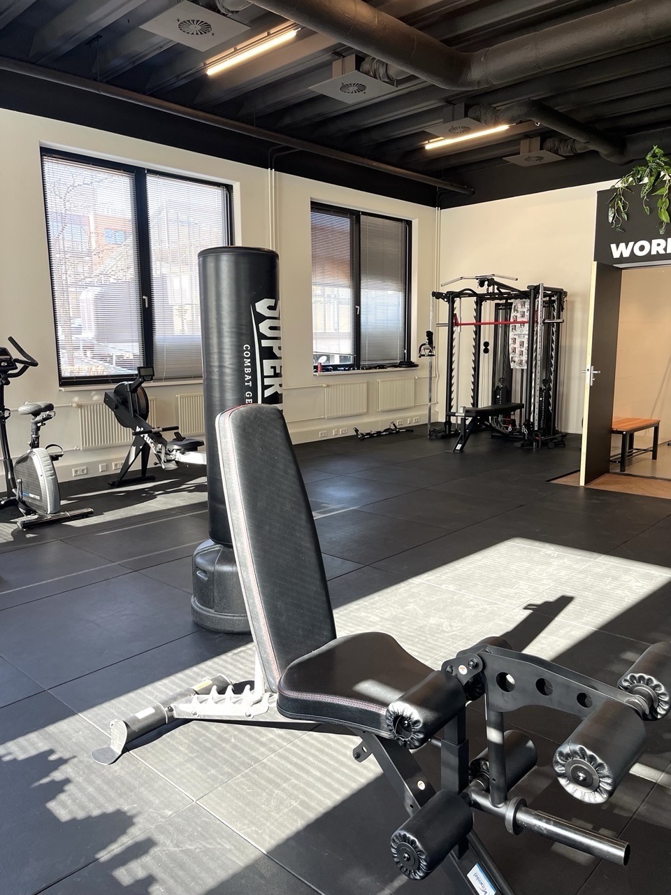 Moderne en ruime sportschool met fitnessapparatuur, een boksdummy en veel natuurlijk licht.
