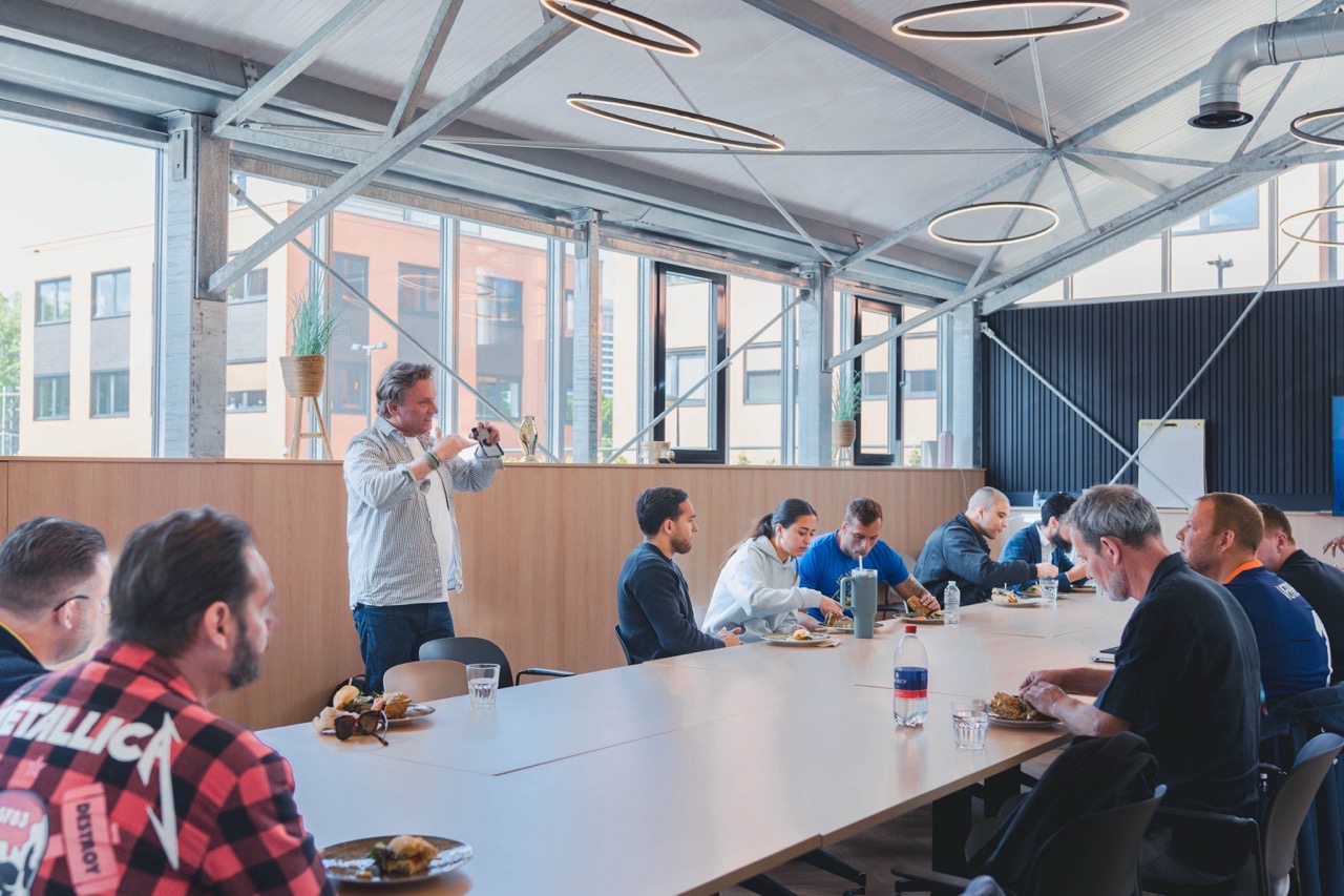 Een groep mensen luncht samen aan een lange tafel in een moderne kantoorruimte tijdens het Campus Offices AI Lunch-event op 8 mei.