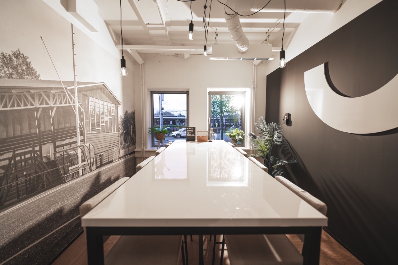 Moderne vergaderruimte met lange witte tafel, muurdecoratie en grote ramen met zicht op buiten.