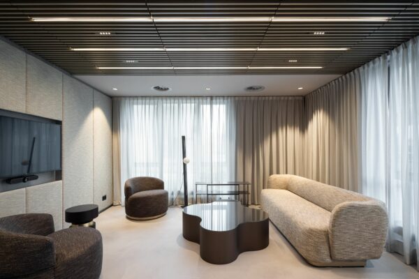 Modern ingerichte lounge met designmeubels, zachte verlichting en een golvend vormgegeven salontafel.
