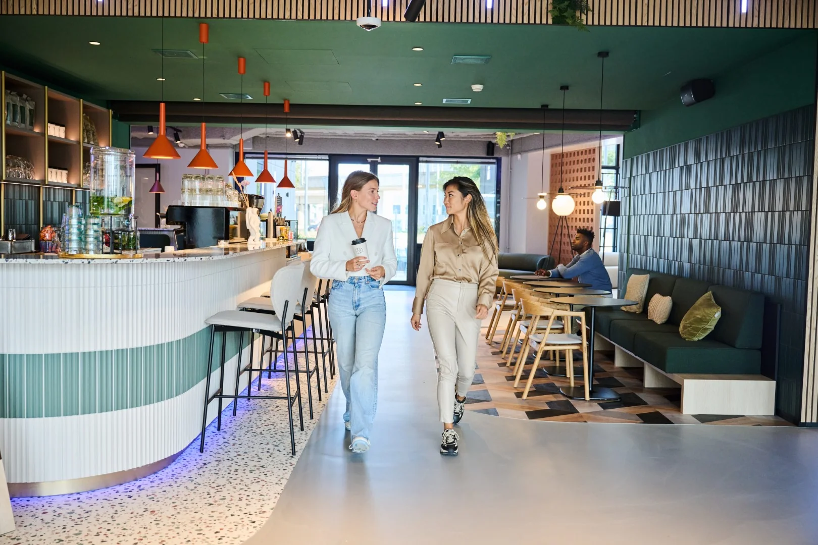 Twee vrouwen lopen pratend door een modern ingerichte koffiebar met zitgedeelte.