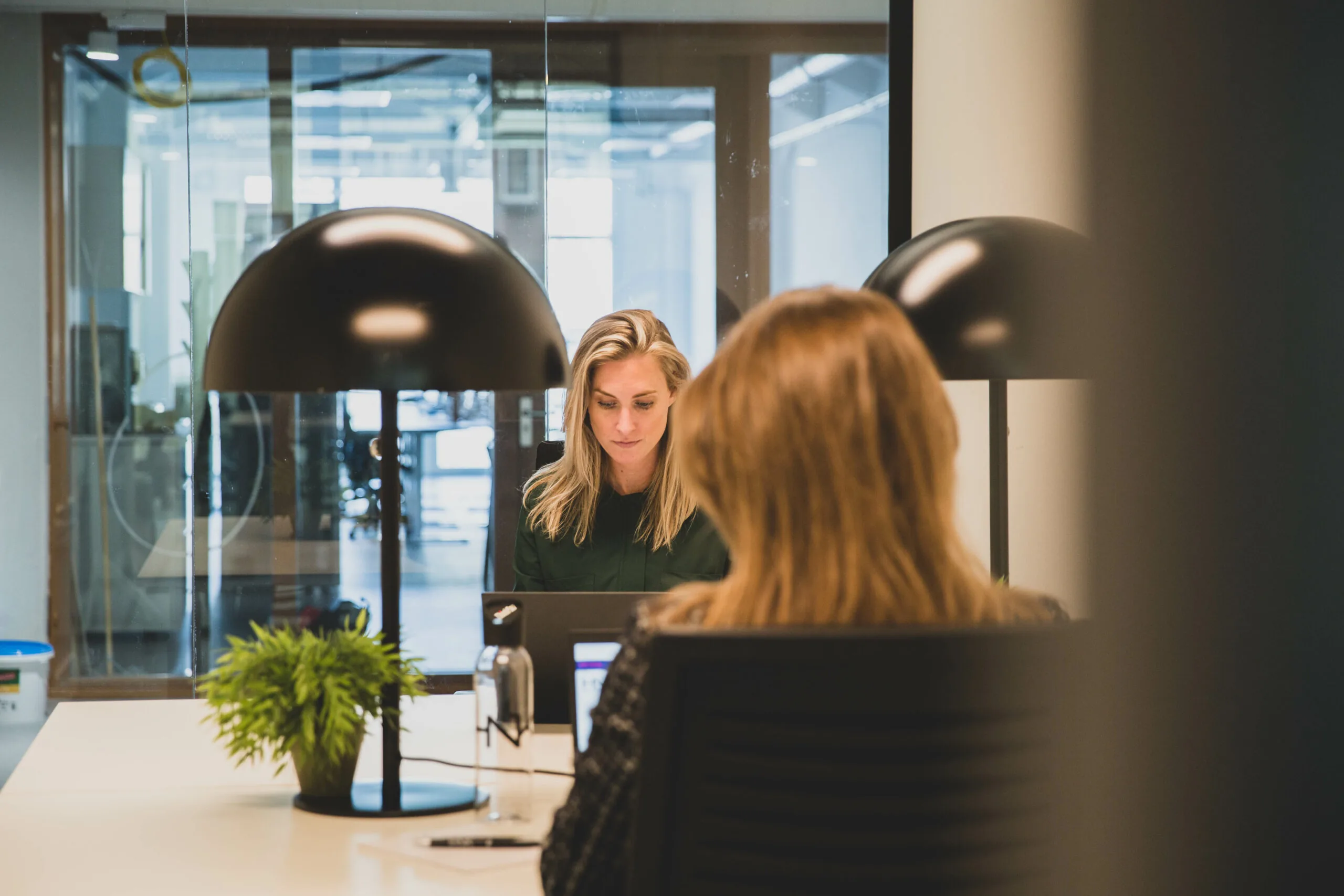 Twee vrouwen werken geconcentreerd op laptops in een moderne kantoorruimte bij HNK Amsterdam Houthavens.