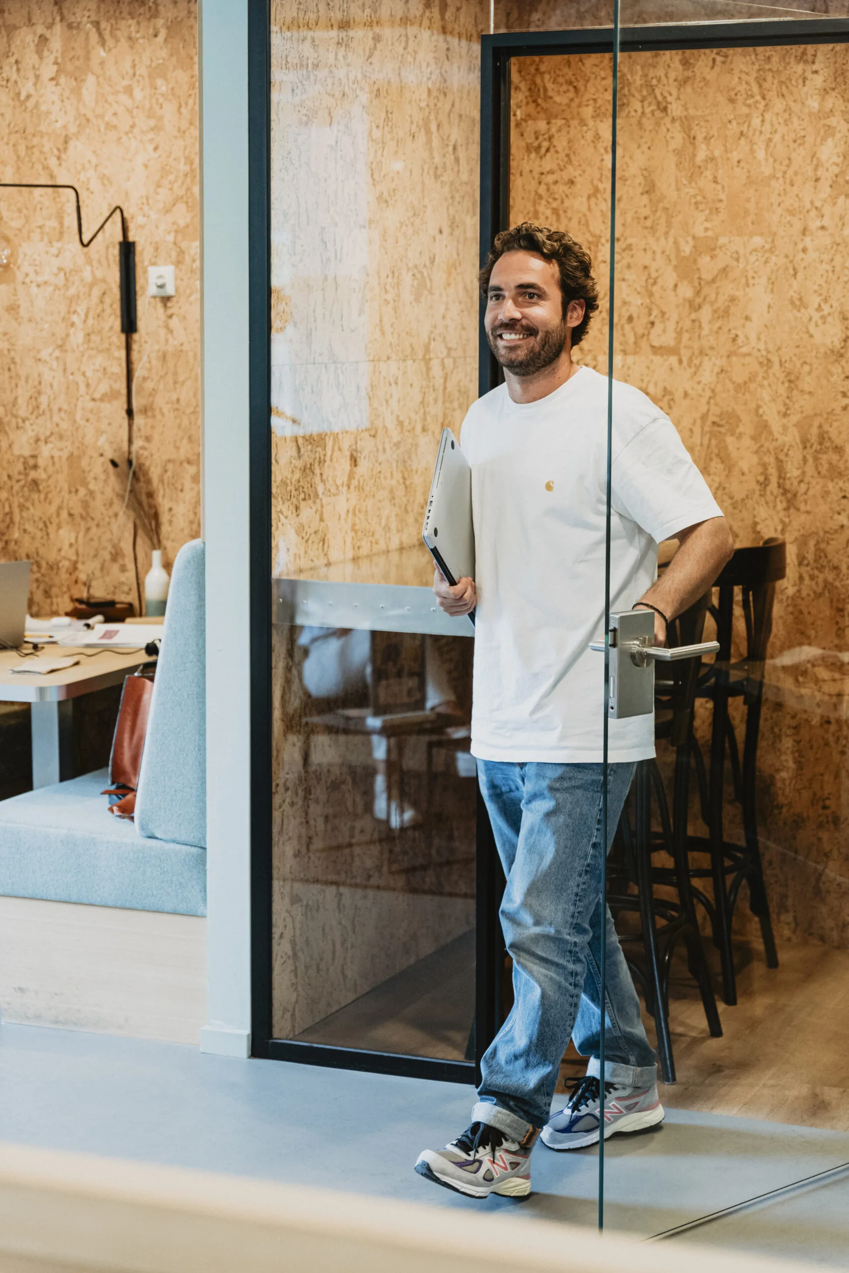 Man met laptop verlaat glimlachend een vergaderruimte in HNK Amsterdam Schinkel.
