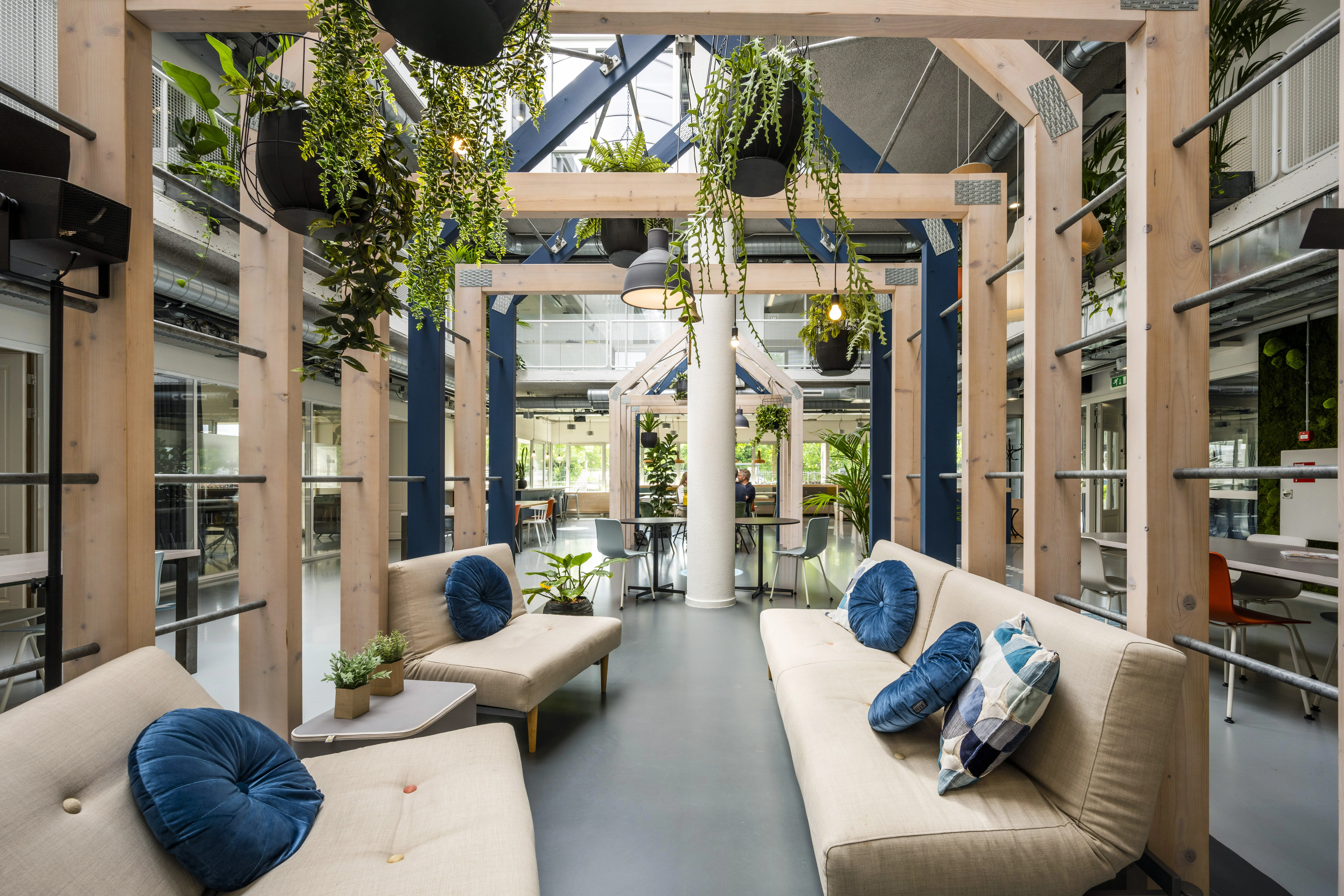 Moderne lounge- en werkruimte in HNK Utrecht West met houten structuren, planten en comfortabele zitplekken.