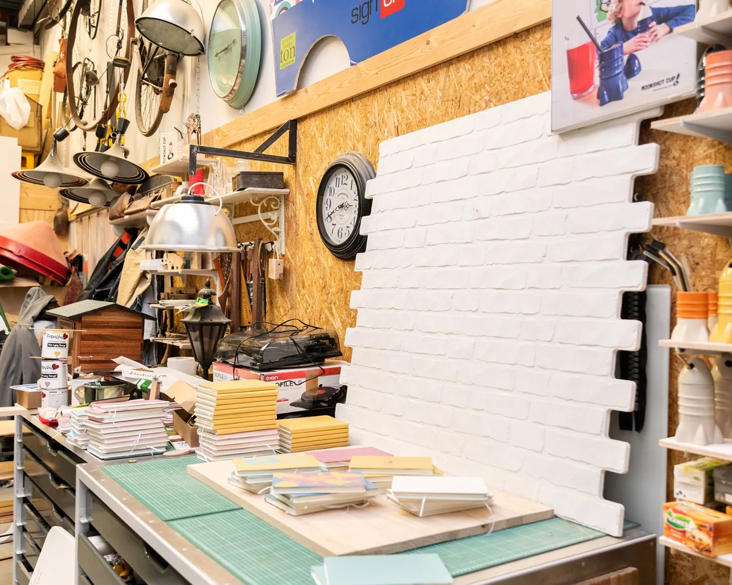 Creatieve en rommelige werkplaats in Steiger 24, Almere, met stapels notitieboekjes, verfpotten en decoratieve objecten.