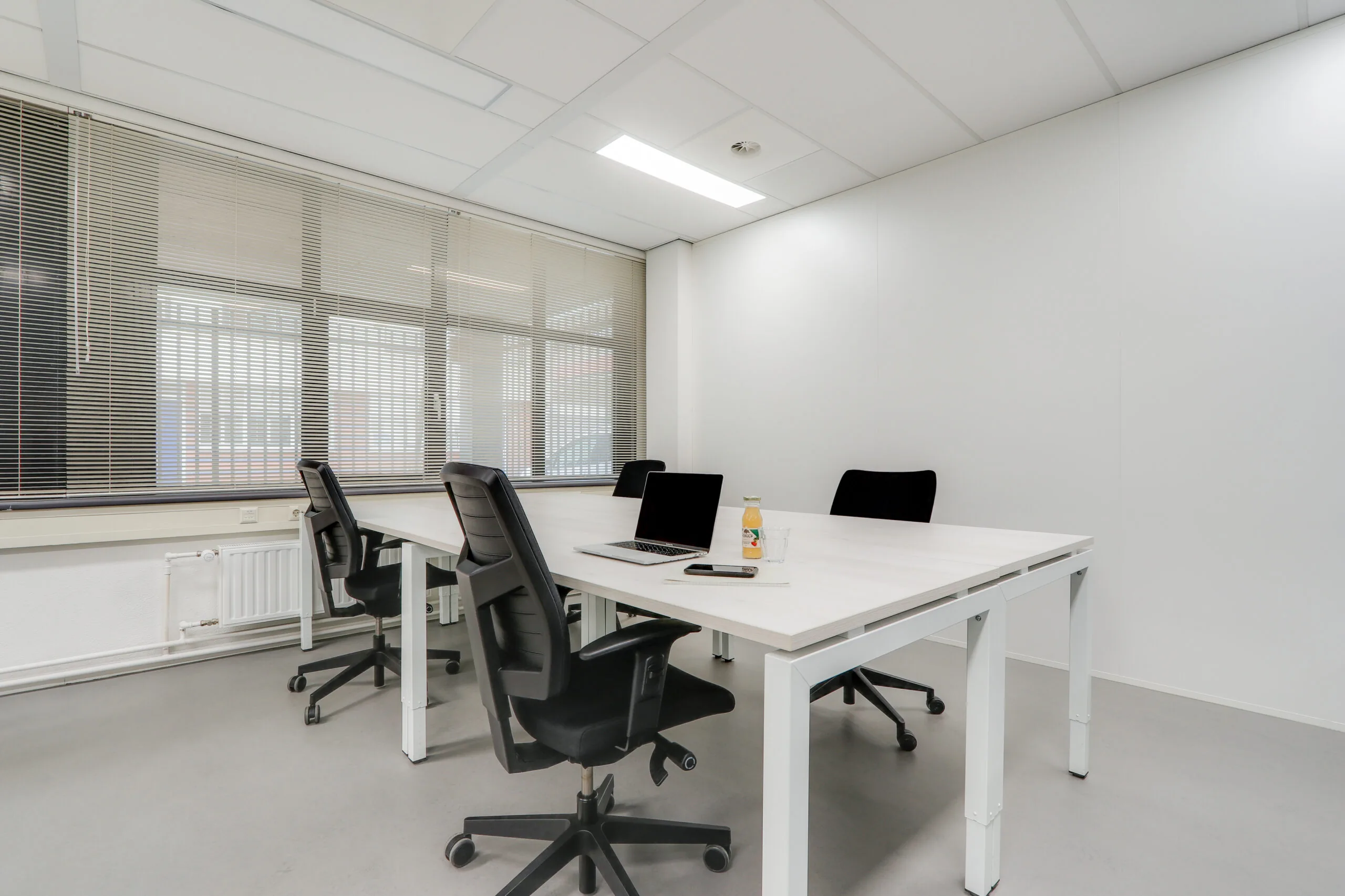 Moderne en lichte kantoorruimte in Rotterdam Centrum met vier bureaustoelen, een laptop en werkbenodigdheden op het bureau.