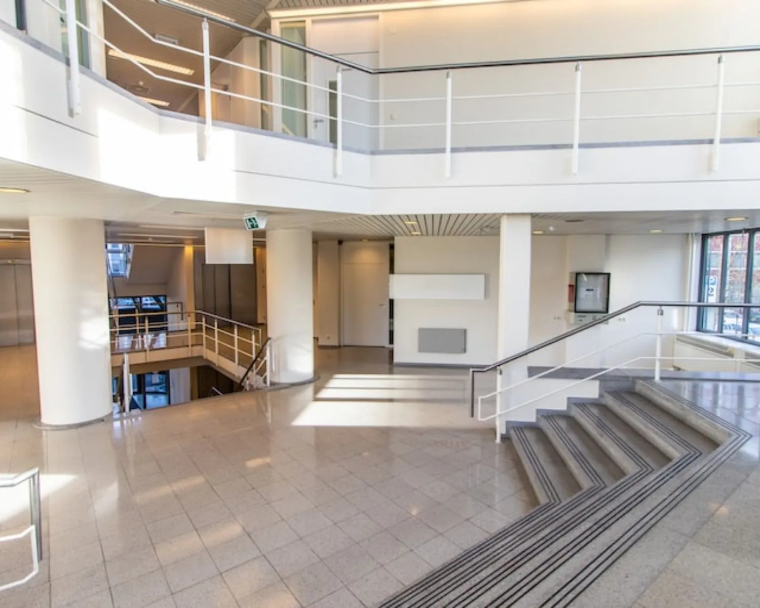 Moderne en lichte entreehal van een kantoorpand aan de Gaetano Martinolaan 75-95 in Maastricht met trappen, balustrades en grote ramen.