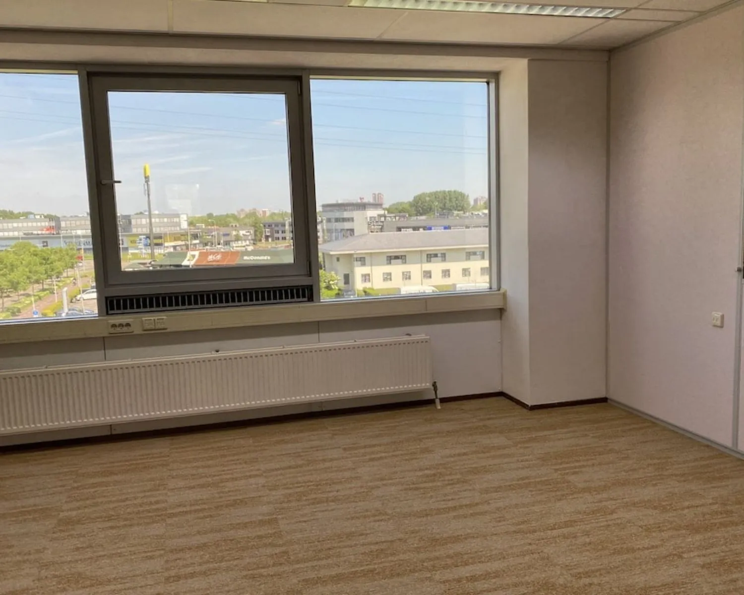 Lichte, lege kantoorruimte met groot raam en uitzicht op bedrijventerrein aan de Kamerlingh Onnesweg 10 in Barendrecht.