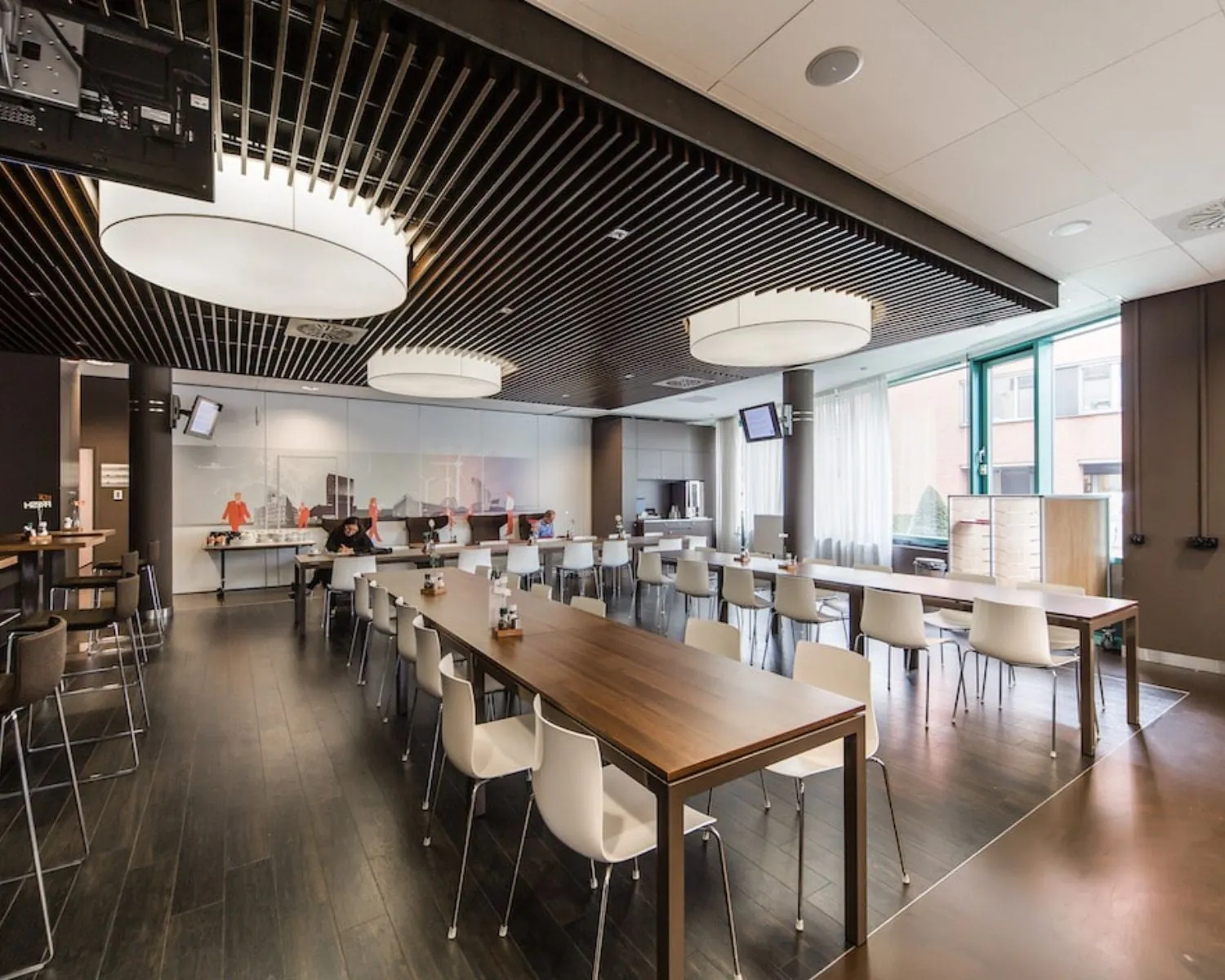 Moderne bedrijfsrestaurant met houten tafels, witte stoelen en grote ronde plafondlampen in kantoorruimte aan de Kronenburgsingel 525 in Arnhem.