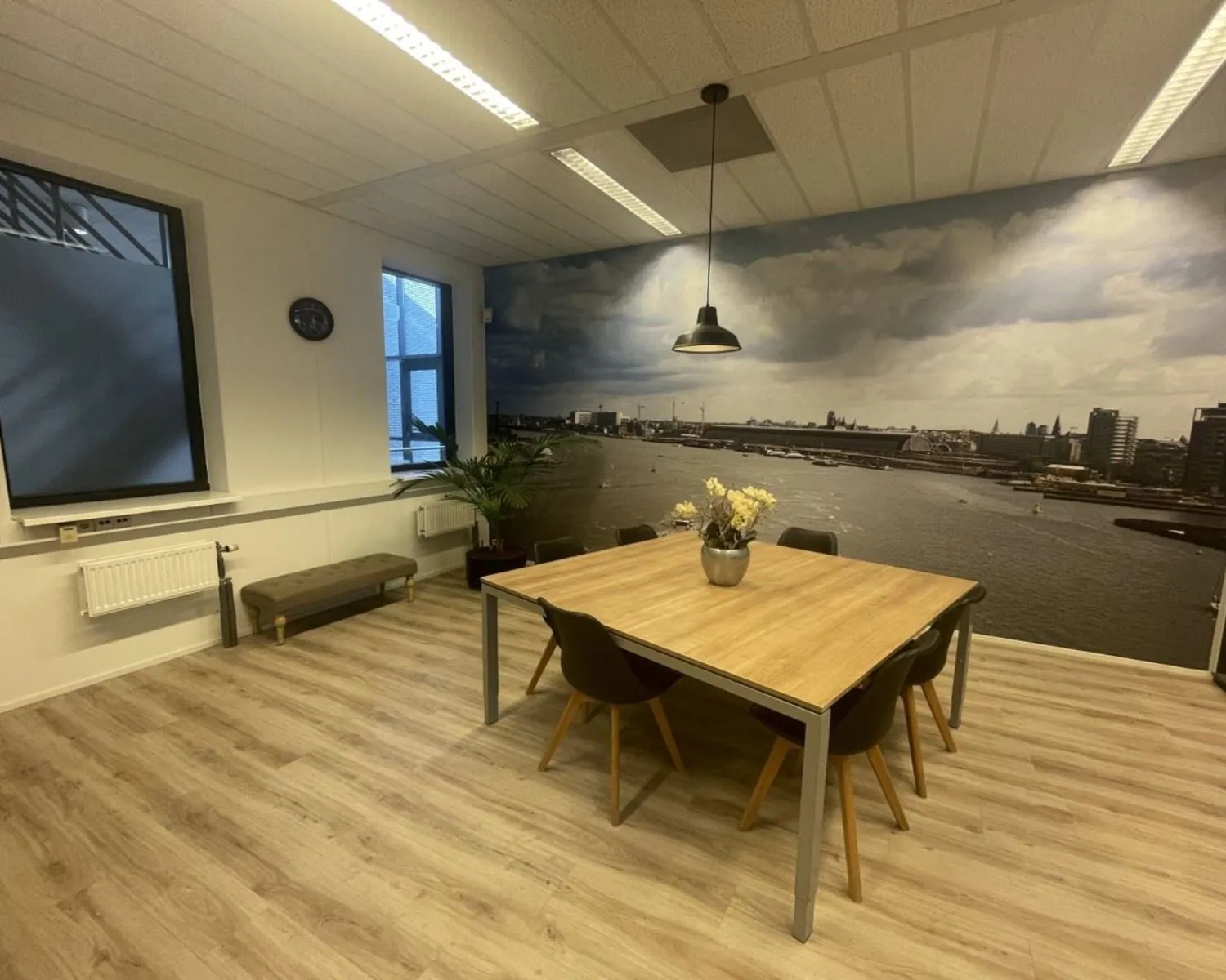 Moderne kantoorruimte aan de Zekeringstraat 17 in Amsterdam met houten vloer, vergadertafel en een wand met fotobehang van de skyline van Amsterdam.