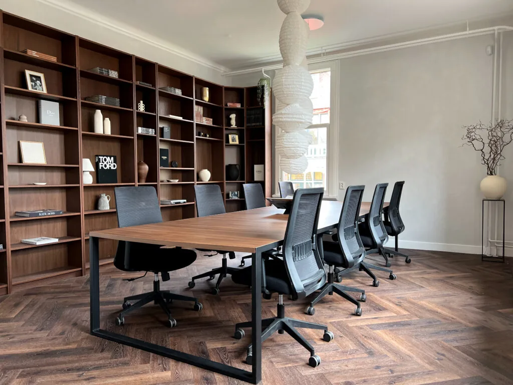 Stijlvolle vergaderruimte bij Creativegrounds aan de Emmalaan met lange houten tafel, moderne bureaustoelen en een wand met open boekenkast.