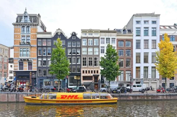 Een DHL-bezorgboot vaart over de Herengracht in Amsterdam langs historische grachtenpanden.