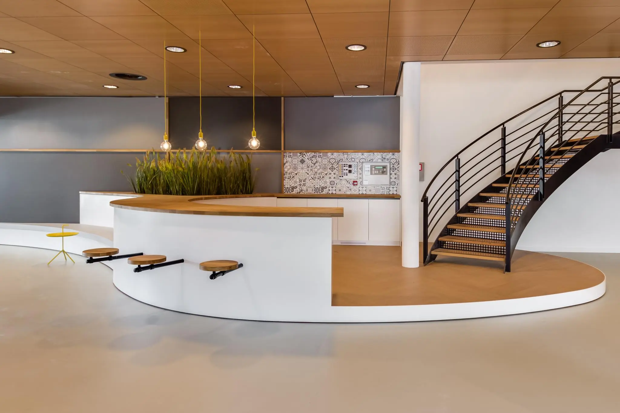 Moderne, open kantoorlobby op het Willemsplein met een ronde balie, hanglampen, ingebouwde zitplaatsen en een stijlvolle wenteltrap.