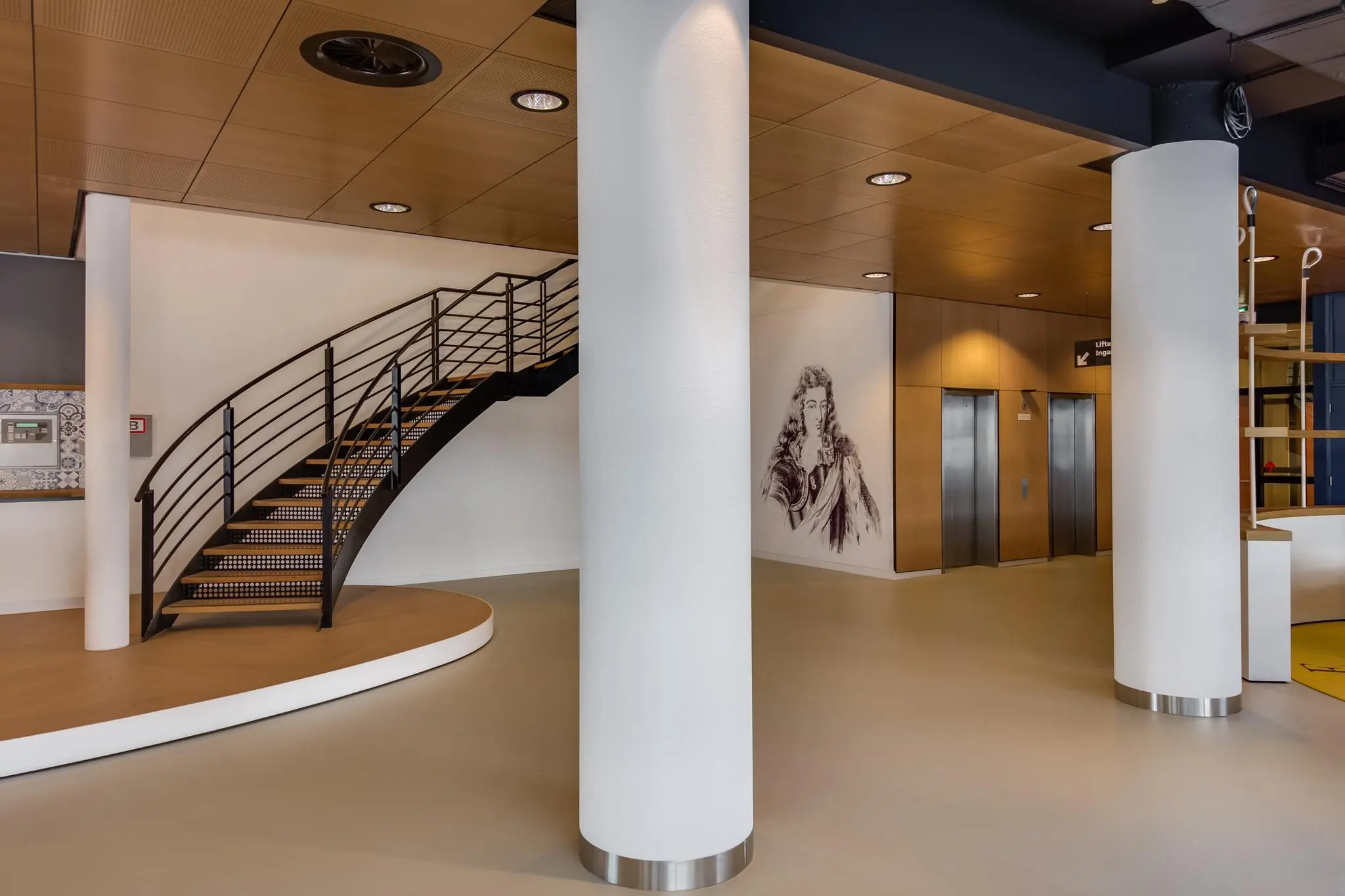Moderne ingangshal aan het Willemsplein met een gebogen trap, muurtekening en liften.