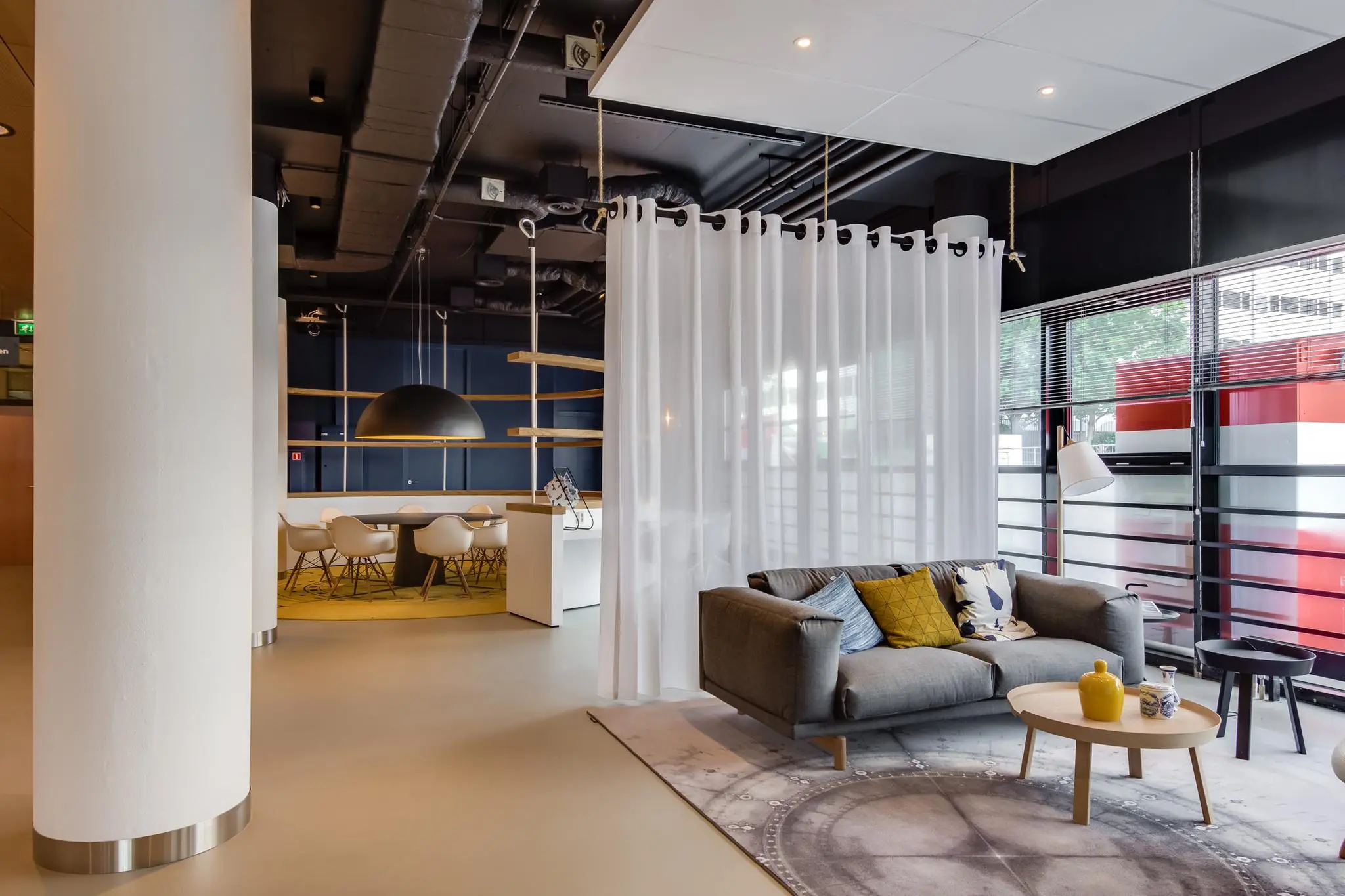 Moderne lounge- en vergaderruimte op het Willemsplein met designmeubilair, scheidingsgordijn en grote ramen.