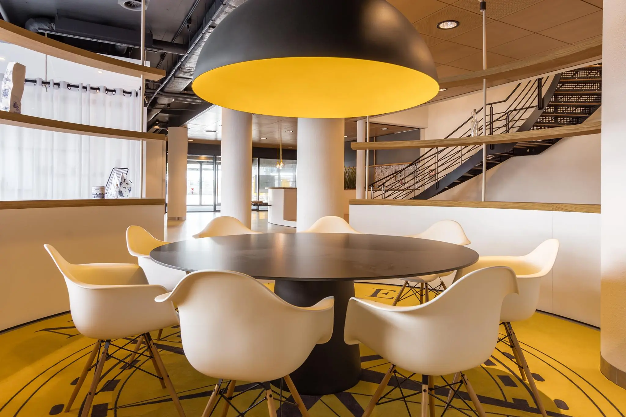 Moderne vergaderruimte op het Willemsplein met ronde tafel, witte stoelen en opvallende gele hanglamp.